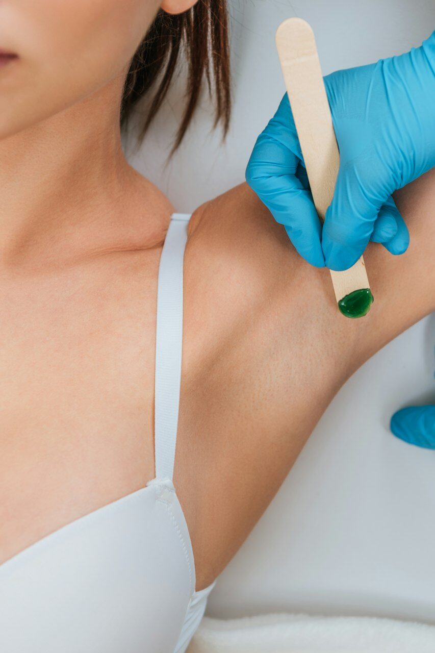 Cropped view of cosmetologist using putty knife for armpit wax depilation